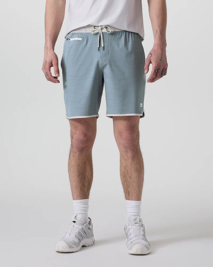 A person standing and wearing Vuori Banks Shorts in a gray color with a drawstring waist and a 7-inch inseam.