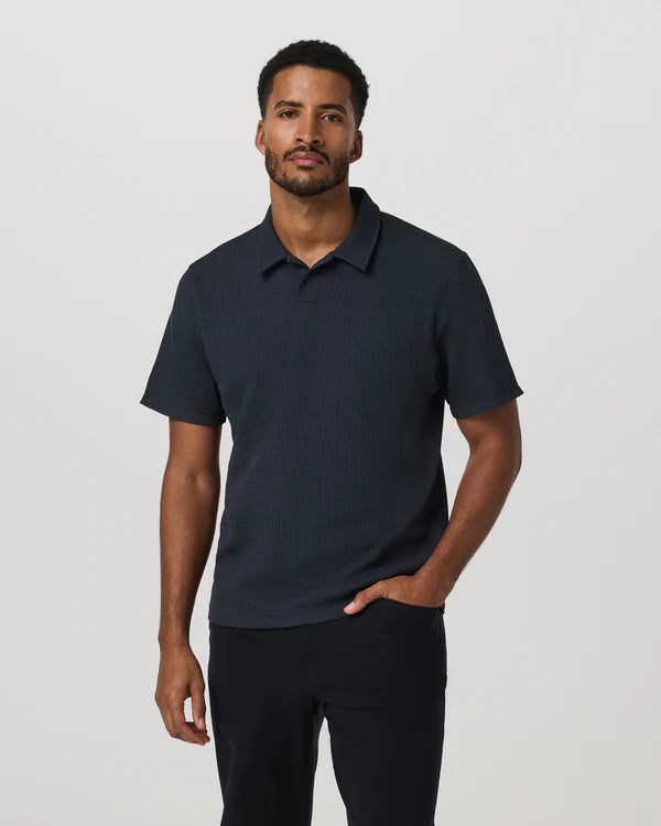 Man wearing a navy Vuori polo shirt against a plain background
