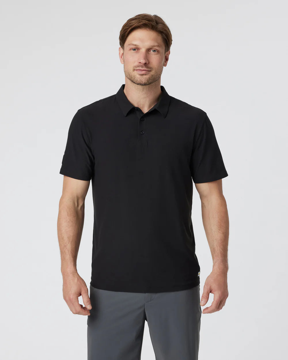 Man wearing a Vuori - Strato Tech Polo in Black and gray pants on a light gray background