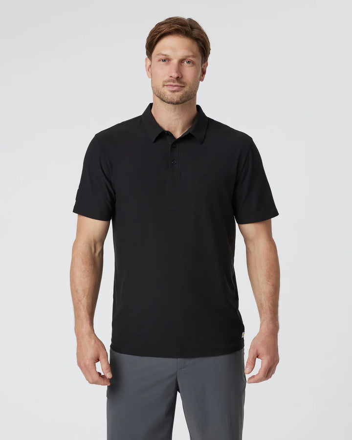 Man wearing a Vuori - Strato Tech Polo in Black and gray pants on a light gray background