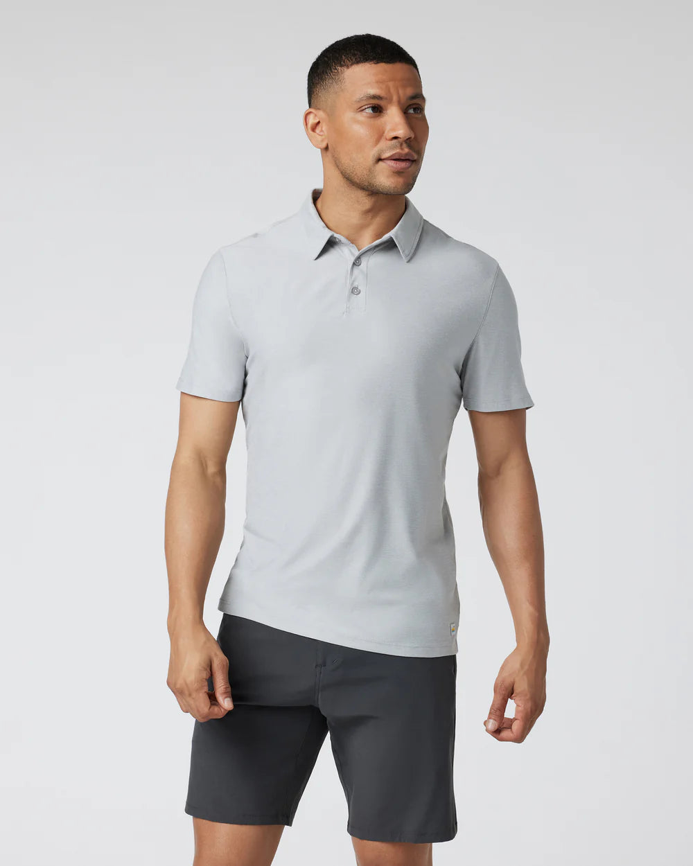 A man wearing a Vuori - Strato Tech Polo in Platinum Heather with short sleeves and a collar.