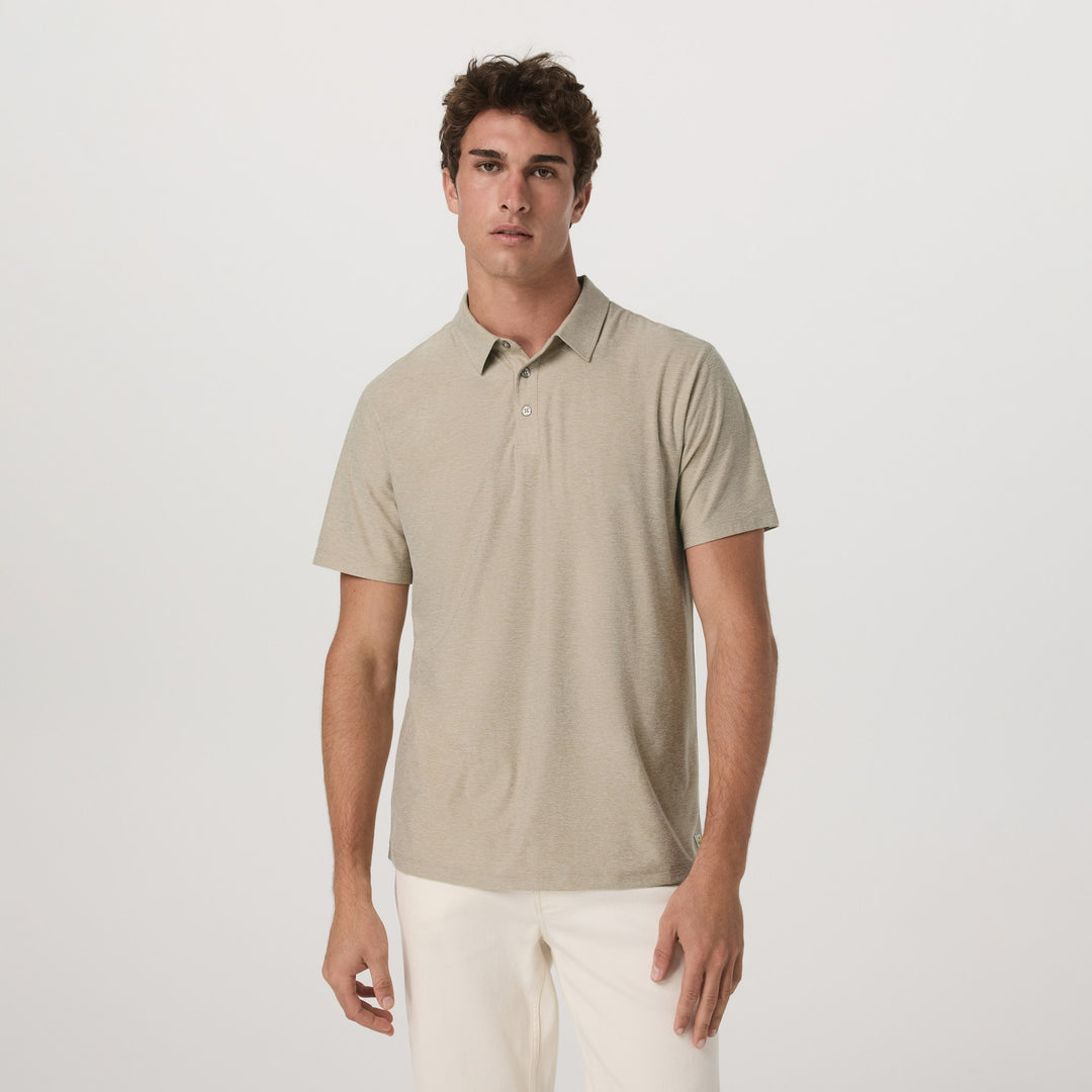 Man wearing a Vuori - Strato Tech Poloand white pants on a light gray background