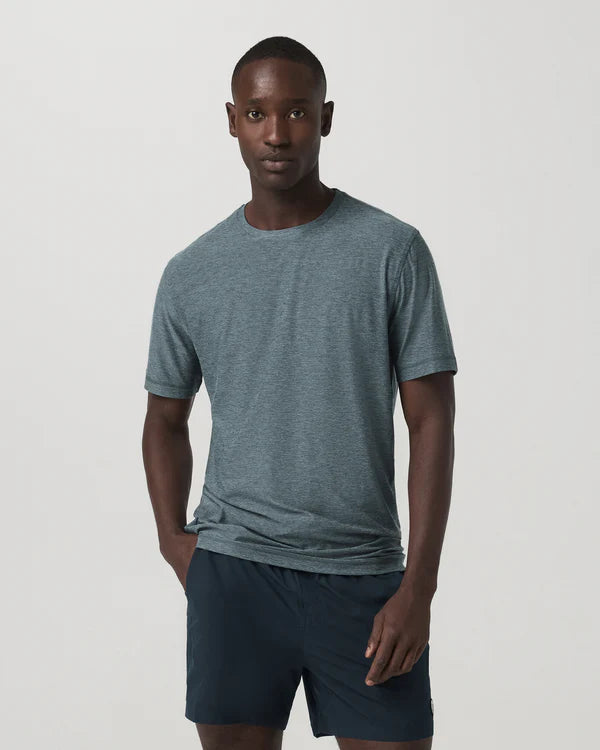 Man wearing a Vuori - Strato Tech Tee and dark shorts on a light gray background
