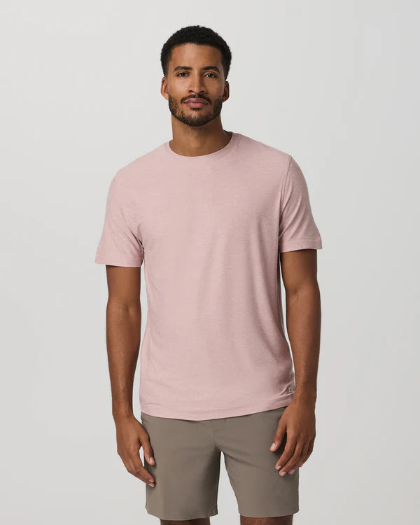 Man wearing a Vuori - Strato Tech Tee in Faded Rose and beige shorts on a plain background