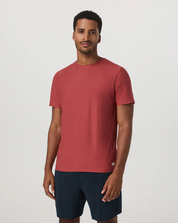 Man wearing a Vuori - Strato Tech Tee in Fire and navy shorts on a white background