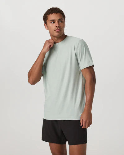 Man wearing a Vuori - Strato Tech Tee in Storm Blue and black shorts on a white background