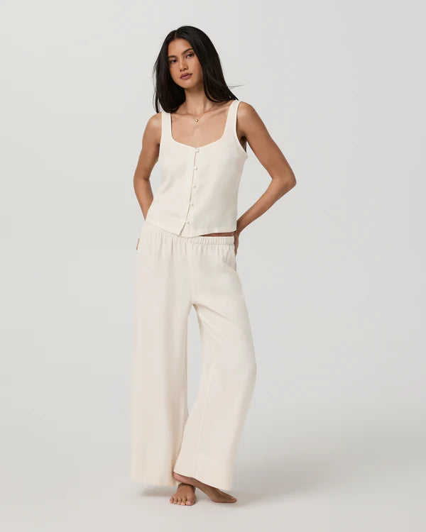Woman wearing a white sleeveless top and wide-leg pants on a plain background