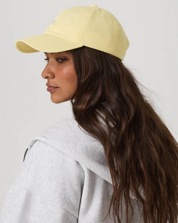 Woman wearing a light yellow Vuori Dad Hat and gray hoodie 
