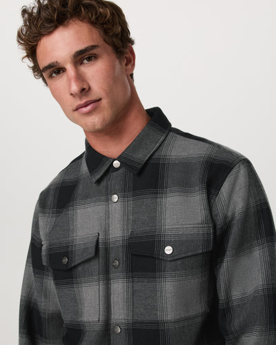 Man wearing a black and gray plaid Vuori Range Shirt Jacket 2.0 against a plain background 